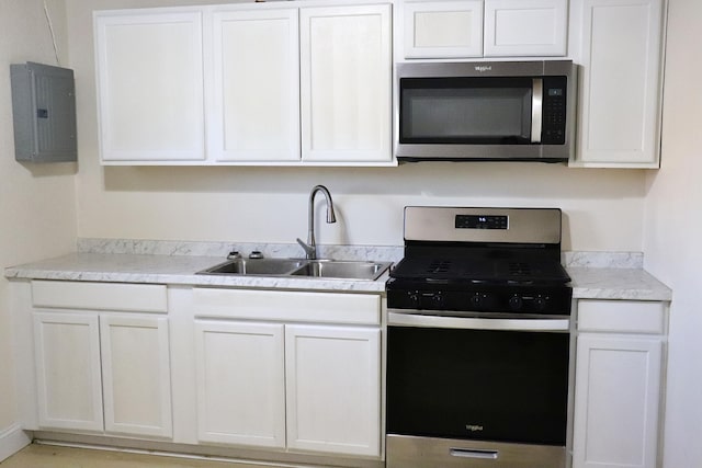 kitchen with a sink, electric panel, appliances with stainless steel finishes, light countertops, and white cabinetry