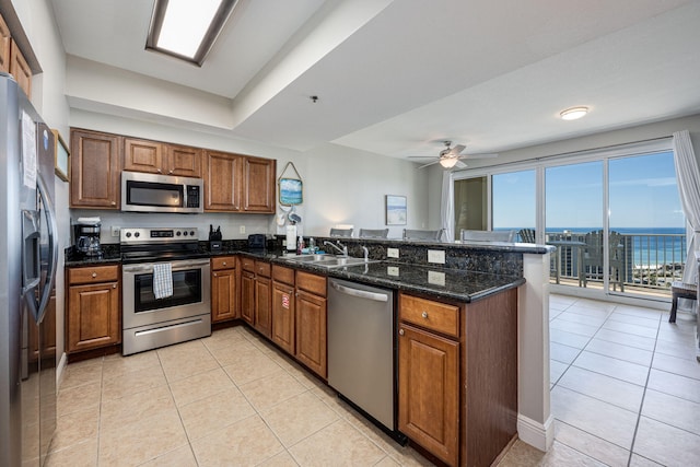 kitchen featuring kitchen peninsula, ceiling fan, dark stone counters, stainless steel appliances, and a water view