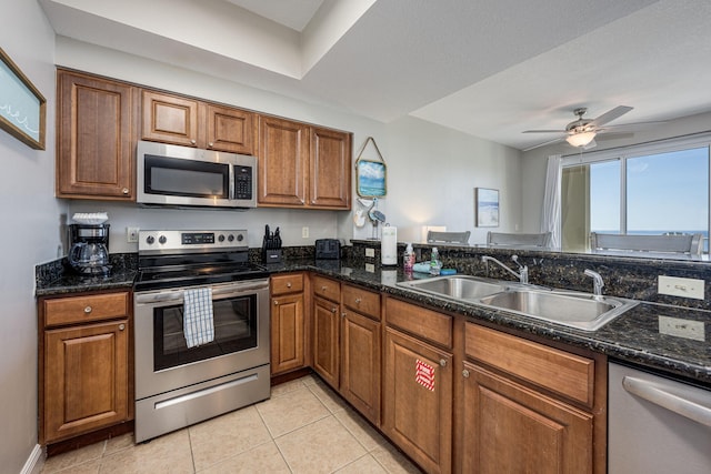 kitchen with sink, ceiling fan, stainless steel appliances, dark stone counters, and light tile patterned floors