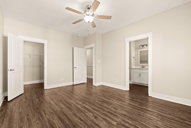 unfurnished bedroom featuring a walk in closet, ensuite bath, a closet, ceiling fan, and dark wood-type flooring