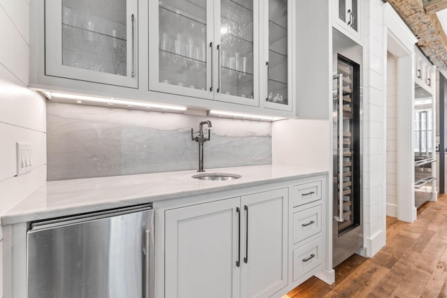 bar featuring light stone countertops, sink, white cabinets, stainless steel refrigerator, and light hardwood / wood-style flooring