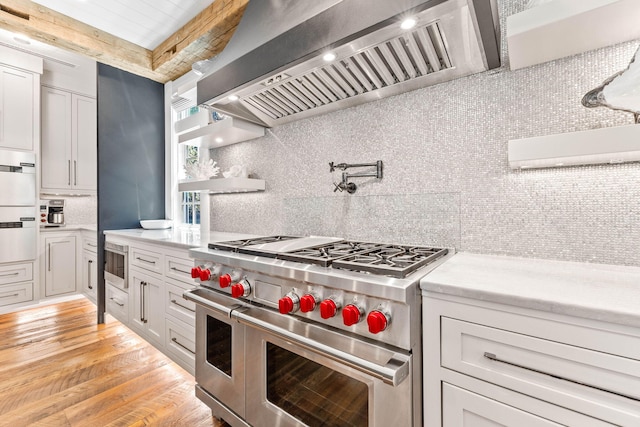 kitchen with ventilation hood, light hardwood / wood-style flooring, decorative backsplash, and stainless steel appliances