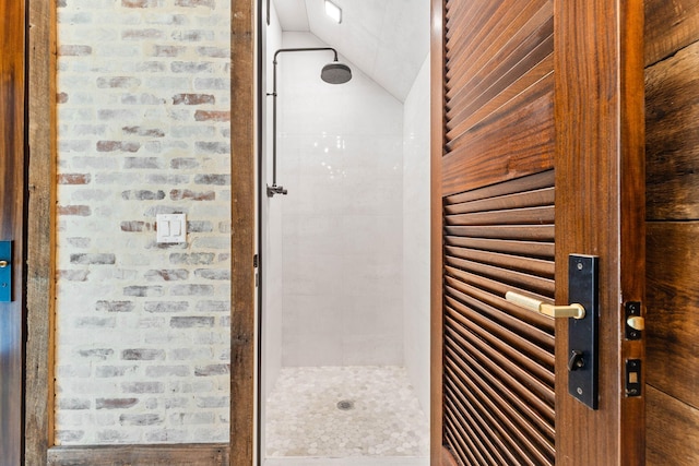 bathroom featuring brick wall, lofted ceiling, and tiled shower