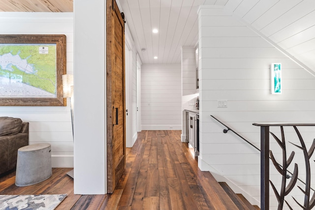 hall with wood walls, dark hardwood / wood-style floors, a barn door, and vaulted ceiling