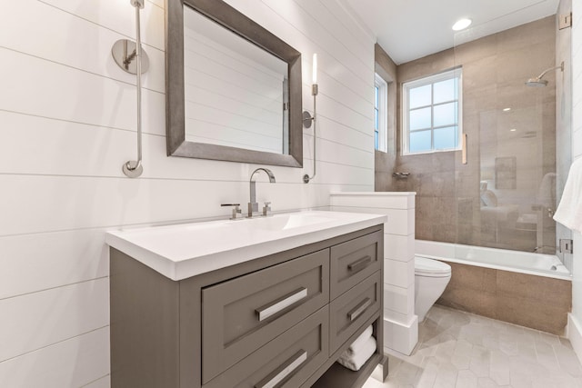 full bathroom featuring tile walls, toilet, vanity, tiled shower / bath combo, and tile patterned flooring