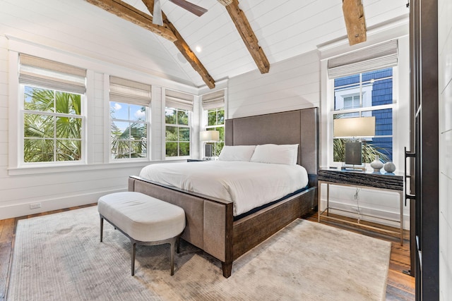 bedroom with vaulted ceiling with beams, light hardwood / wood-style flooring, wooden walls, and ceiling fan