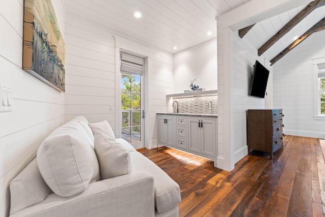 living room with sink, lofted ceiling with beams, dark hardwood / wood-style floors, and wood walls