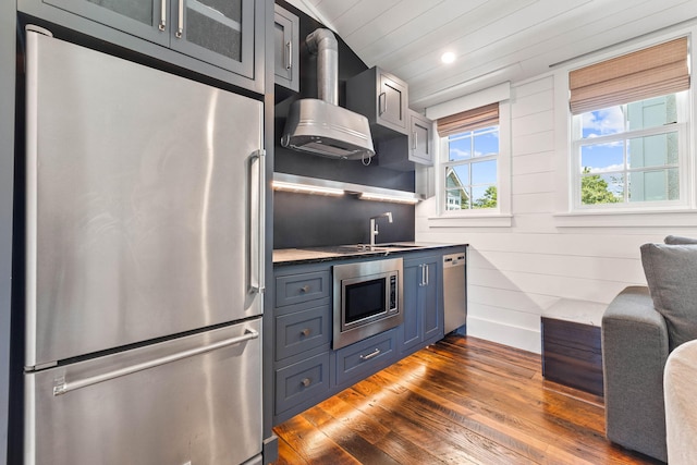 kitchen with appliances with stainless steel finishes, sink, blue cabinets, dark hardwood / wood-style floors, and ventilation hood