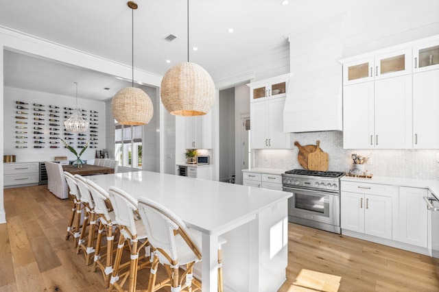 kitchen featuring white cabinets, a kitchen island, a breakfast bar, decorative light fixtures, and high end range