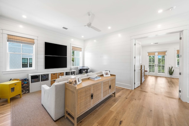 living room with ceiling fan, light wood-type flooring, and wooden walls