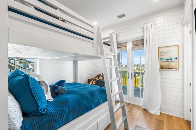 bedroom with light hardwood / wood-style flooring, multiple windows, wood walls, and french doors