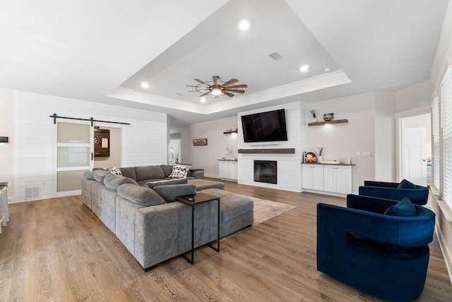 living room featuring light hardwood / wood-style floors, a barn door, a large fireplace, and a raised ceiling