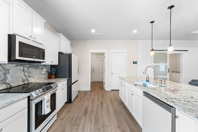 kitchen featuring hanging light fixtures, stainless steel appliances, tasteful backsplash, white cabinetry, and wood walls