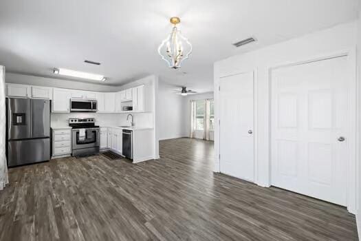 kitchen featuring dark wood-type flooring, hanging light fixtures, white cabinetry, appliances with stainless steel finishes, and ceiling fan with notable chandelier