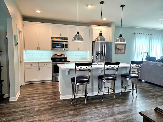 kitchen featuring appliances with stainless steel finishes, pendant lighting, white cabinets, dark hardwood / wood-style floors, and a kitchen island with sink