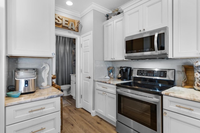 kitchen featuring decorative backsplash, light wood-style floors, appliances with stainless steel finishes, ornamental molding, and white cabinetry
