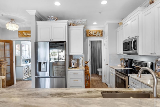 kitchen with appliances with stainless steel finishes, light stone countertops, ornamental molding, and a sink