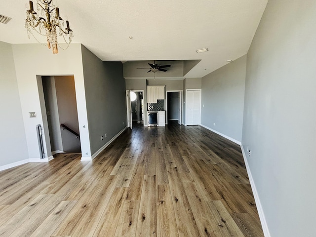 unfurnished living room featuring baseboards, visible vents, wood finished floors, and ceiling fan with notable chandelier