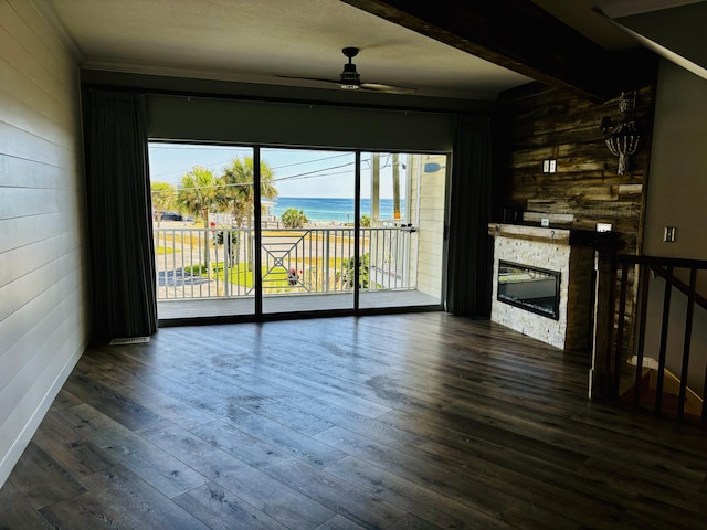 interior space with a stone fireplace, wooden walls, a ceiling fan, and a water view