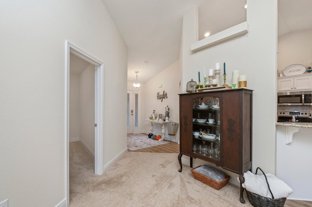 hallway with baseboards, light carpet, and lofted ceiling