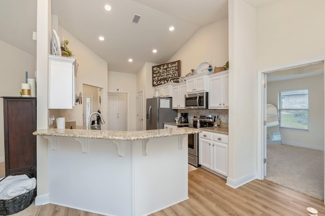 kitchen with a peninsula, a breakfast bar area, white cabinets, light stone counters, and appliances with stainless steel finishes