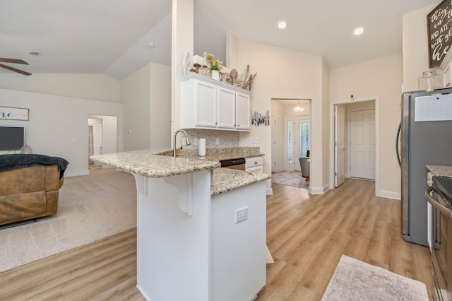 kitchen with light stone countertops, white cabinets, a peninsula, open floor plan, and lofted ceiling