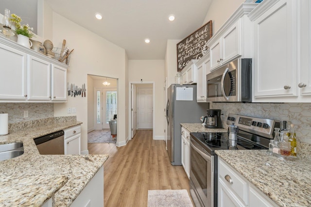 kitchen with light wood-type flooring, white cabinetry, stainless steel appliances, light stone counters, and decorative backsplash