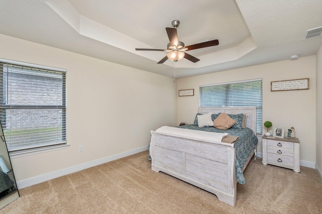 carpeted bedroom with ceiling fan, a tray ceiling, visible vents, and baseboards