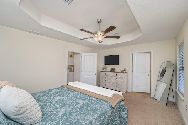 bedroom featuring visible vents, baseboards, a tray ceiling, and light carpet