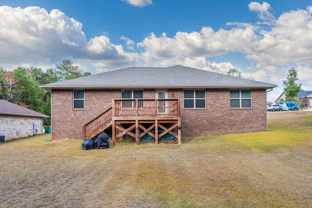 rear view of house with brick siding, a shingled roof, a yard, and a deck