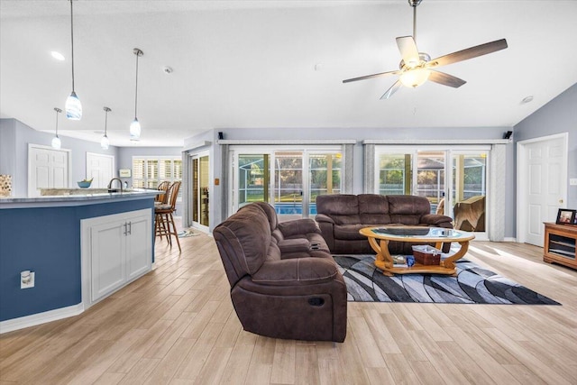 living room with light wood-type flooring, vaulted ceiling, ceiling fan, and plenty of natural light