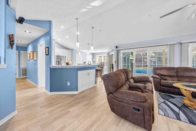 living room with a textured ceiling, sink, high vaulted ceiling, ceiling fan, and light hardwood / wood-style flooring