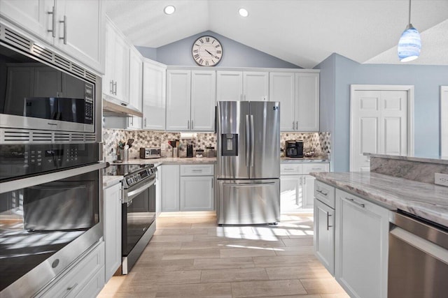 kitchen with tasteful backsplash, white cabinetry, appliances with stainless steel finishes, pendant lighting, and lofted ceiling