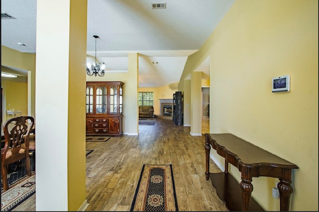 hall featuring hardwood / wood-style flooring, lofted ceiling, an inviting chandelier, and a textured ceiling