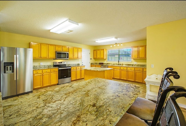 kitchen with light stone counters, stainless steel appliances, a textured ceiling, and a kitchen island