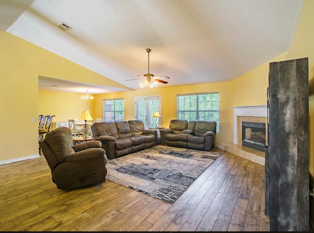 living room featuring a tile fireplace, hardwood / wood-style floors, vaulted ceiling, a textured ceiling, and ceiling fan with notable chandelier