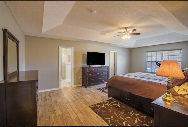 bedroom with ceiling fan, a textured ceiling, light wood-type flooring, and a raised ceiling