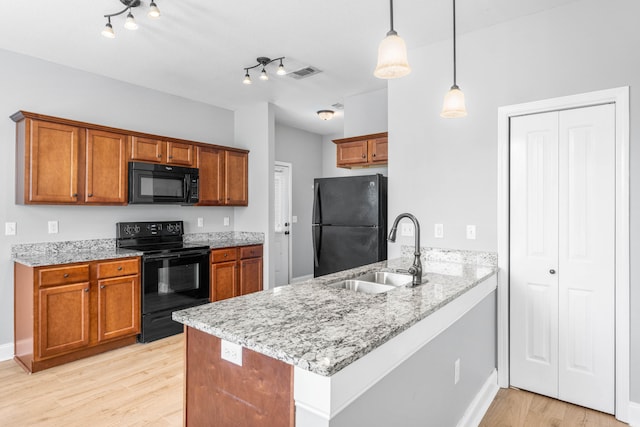 kitchen with black appliances, sink, kitchen peninsula, hanging light fixtures, and light hardwood / wood-style flooring