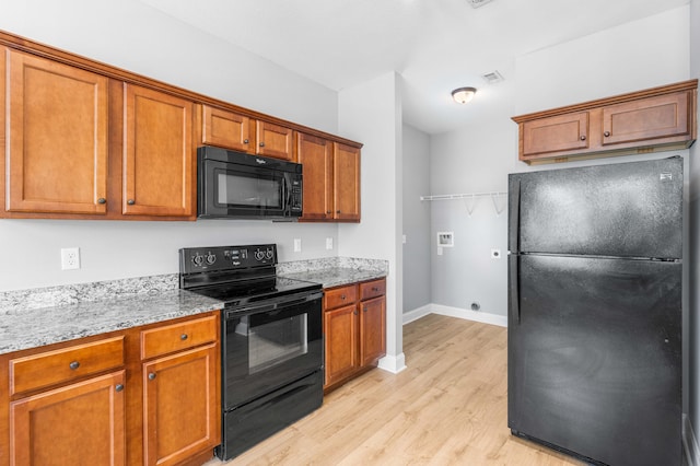 kitchen featuring light stone countertops, black appliances, and light wood-type flooring