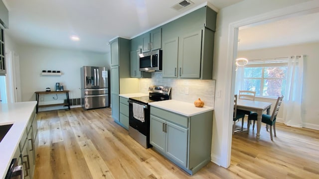 kitchen featuring appliances with stainless steel finishes, decorative backsplash, green cabinetry, and light wood-type flooring