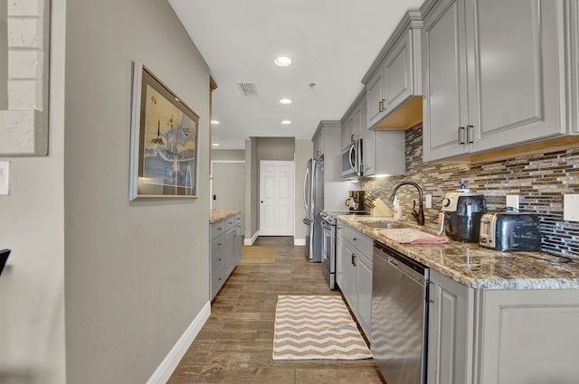 kitchen with light stone counters, appliances with stainless steel finishes, light hardwood / wood-style flooring, gray cabinets, and sink