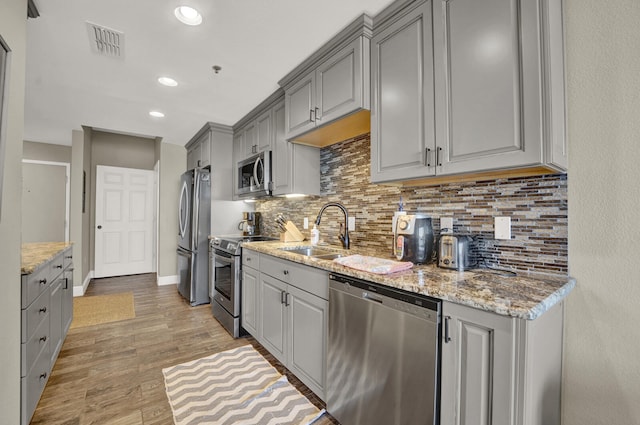 kitchen with gray cabinetry, backsplash, stainless steel appliances, sink, and light wood-type flooring