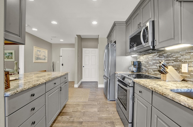 kitchen featuring tasteful backsplash, light stone counters, gray cabinetry, light hardwood / wood-style floors, and stainless steel appliances