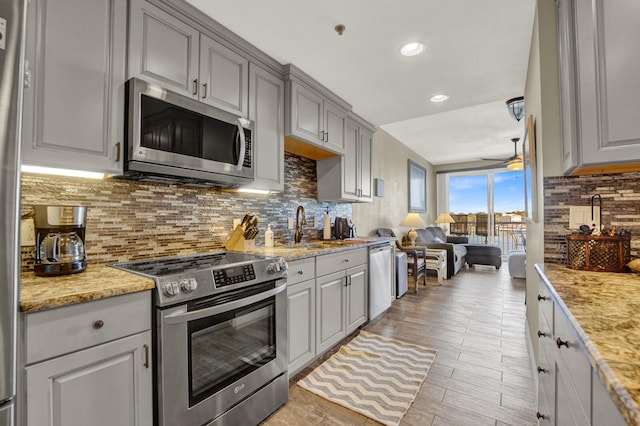 kitchen with ceiling fan, stainless steel appliances, light stone counters, and gray cabinetry