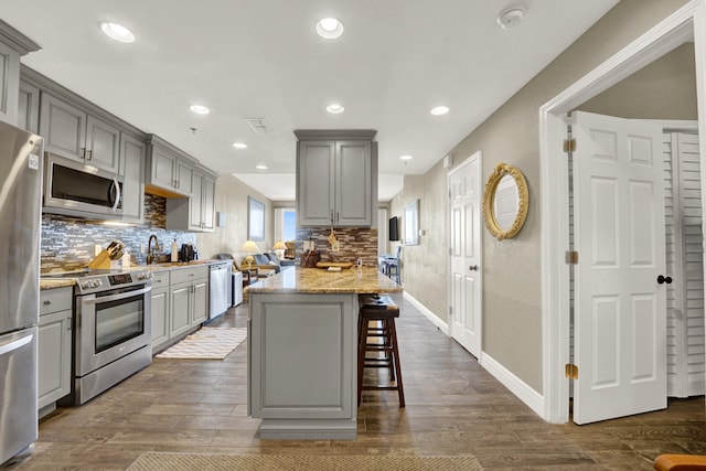 kitchen featuring dark hardwood / wood-style flooring, appliances with stainless steel finishes, gray cabinets, and a kitchen breakfast bar