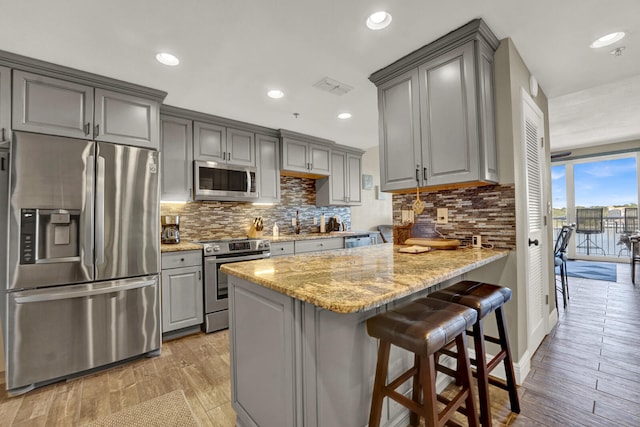 kitchen featuring kitchen peninsula, stainless steel appliances, light stone countertops, and light wood-type flooring