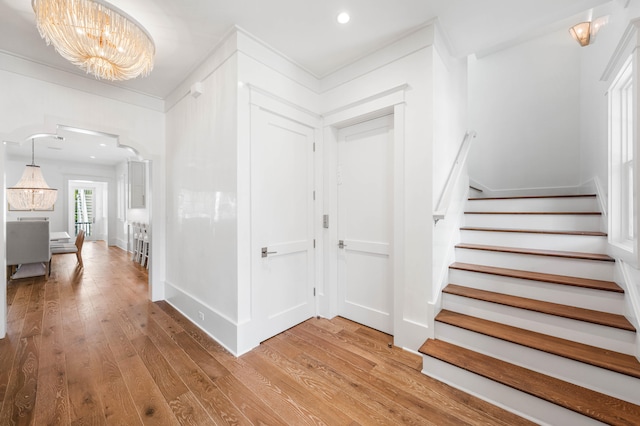 entrance foyer with arched walkways, stairway, light wood-style flooring, and an inviting chandelier