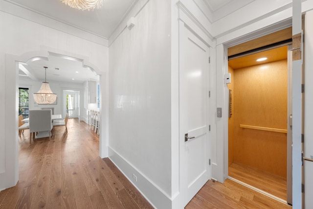 hall with wood finished floors, baseboards, elevator, arched walkways, and ornamental molding