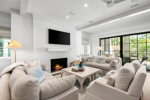 living area with beamed ceiling, recessed lighting, visible vents, and a lit fireplace