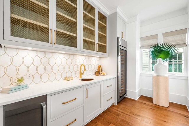 bar with backsplash, beverage cooler, light wood finished floors, and a sink